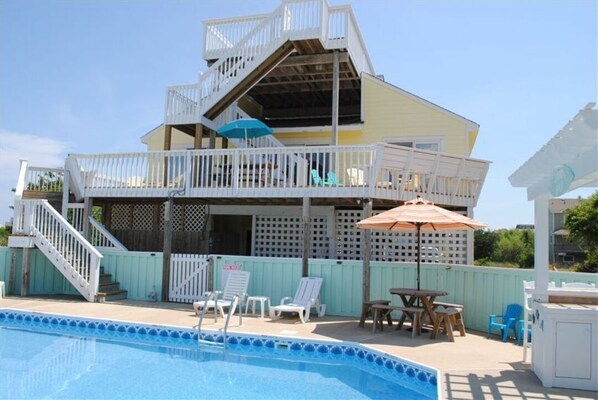 A two-story house with a pool, outdoor furniture, and a wooden deck.