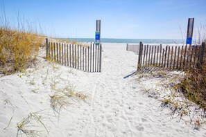A sandy beach path leading to the ocean, flanked by wooden fences and sparse vegetation. - Comfortable condo with two pools, sauna, hot tub, tennis - walk to the beach (Myrtle Beach)