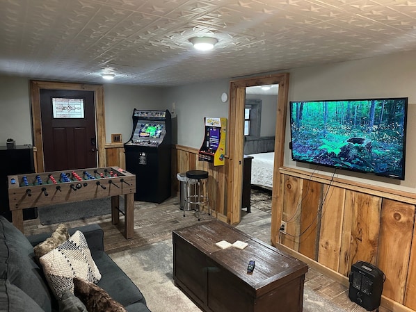 A room with a foosball table, a gaming console, a television, and a bed. - Arcade Cabin Near Parkway | Hot Tub | Pool Access (Pigeon Forge)