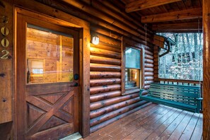 A log cabin with a wooden door, a bench, and a porch with a view of trees. - Arcade Cabin Near Parkway | Hot Tub | Pool Access (Pigeon Forge)