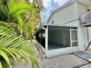 A covered outdoor area with a sliding glass door, surrounded by gravel and palm trees. - 266 S. Harbor - Anna Maria Island- Private home 3 Bedroom/ 2 Bath , maximum occupancy of 6 people. (Holmes Beach)