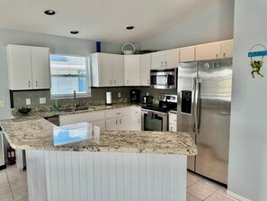 A modern kitchen with white cabinets, a stainless steel refrigerator, a built-in microwave, and a granite countertop island. - 266 S. Harbor - Anna Maria Island- Private home 3 Bedroom/ 2 Bath , maximum occupancy of 6 people. (Holmes Beach)