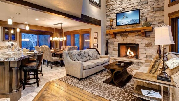 A spacious living area with a stone fireplace, a television mounted on the wall, and a dining area with a large window.