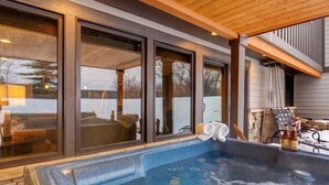 A hot tub area with a stone surround, large windows, and a wooden ceiling.