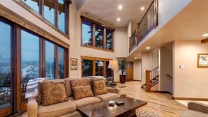 A spacious living room with a large window, a sofa, a coffee table, and a staircase leading to an upper level.