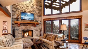 A living room with a stone fireplace, a sofa, a coffee table, and a television mounted on the wall.