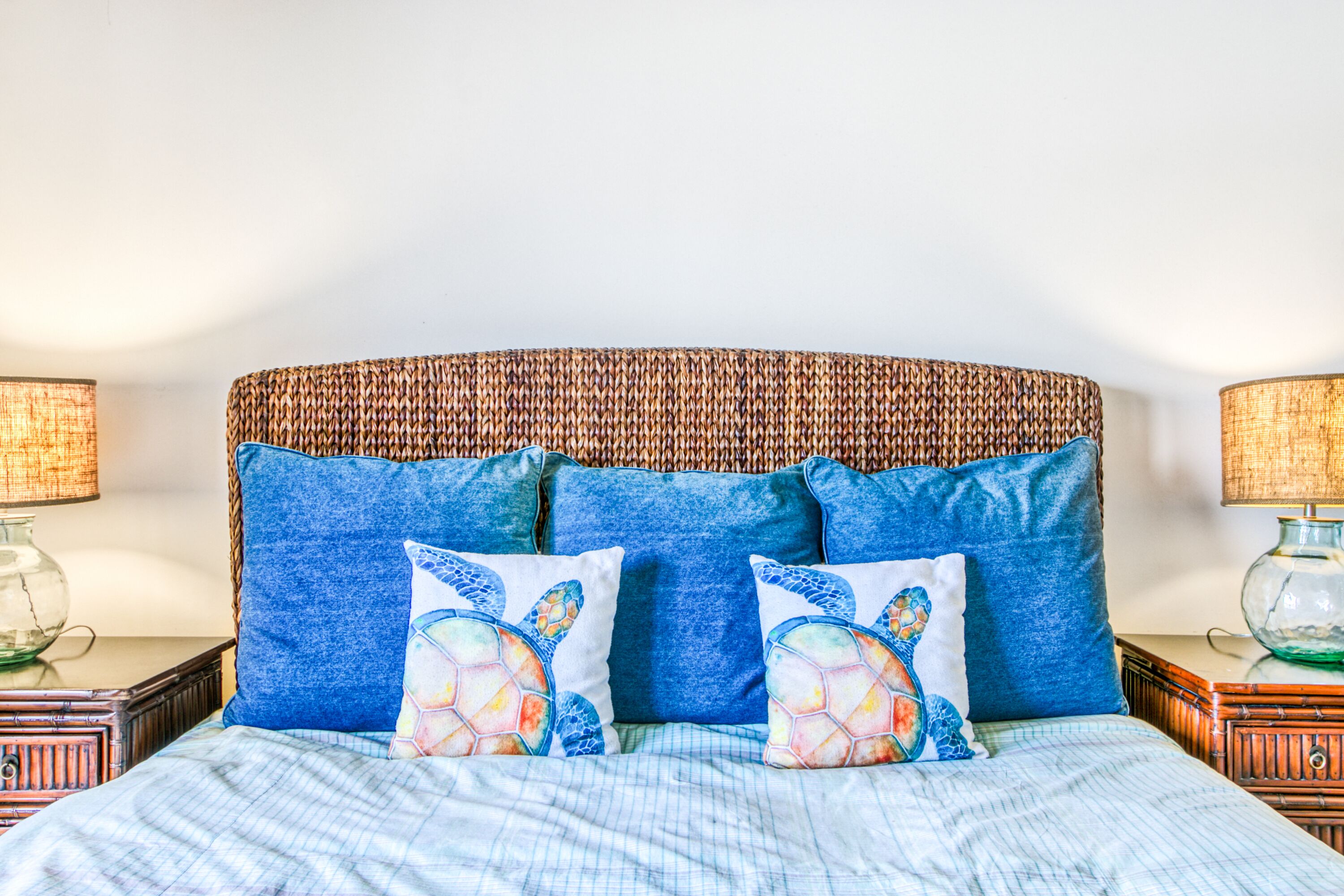 A bed with a woven headboard, blue bedding, and decorative pillows with a turtle design.