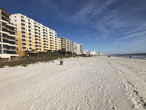 A sandy beach with footprints leading to a building with multiple balconies.