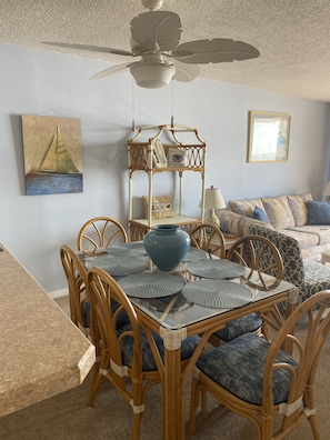 A dining area with a glass table, wicker chairs, and a ceiling fan.