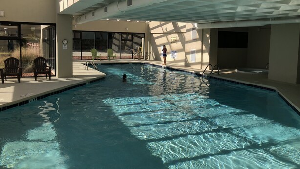 Una piscina interior con agua cristalina, un techo iluminado por el sol y algunas sillas alrededor de la zona de la piscina.