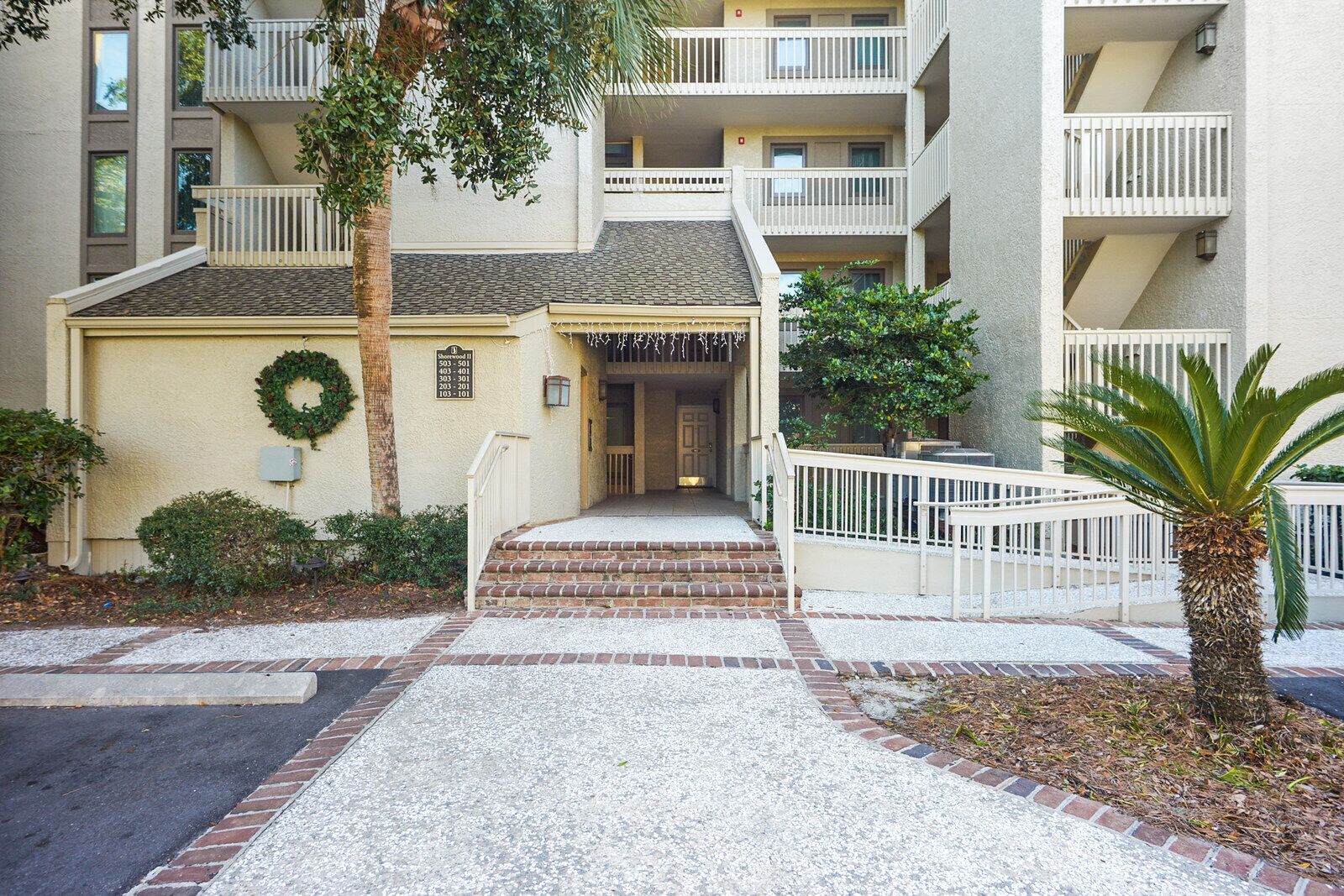 A multi-story residential building with a central entrance, a small porch, and a brick pathway leading to the door.