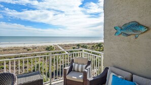 Un balcone con mobili in vimini, un'opera decorativa raffigurante pesci e vista sulla spiaggia e sull'oceano.