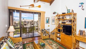 Una sala de estar con un ventanal grande, muebles de mimbre, un televisor y objetos decorativos.