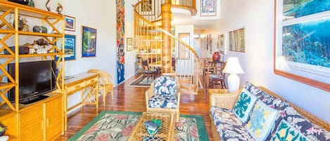 A spacious living room with a wooden staircase, wicker furniture, and a large window with a view.