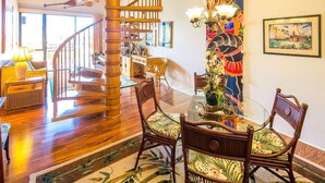 Amplia sala de estar con una escalera de madera, una mesa de comedor de vidrio y sillas con temática tropical.