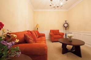 A room with a sofa, armchair, and a small table with a vase of flowers.