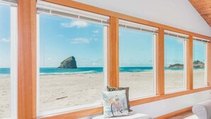 Ein Zimmer mit großen Fenstern mit Blick auf einen Strand, einer gepolsterten Bank und einem Kissen mit Fahrradmotiv.
