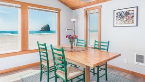 Ein Essbereich mit Holztisch und -stühlen, großen Fenstern mit Blick auf den Strand und einer Decke mit sichtbaren Balken.