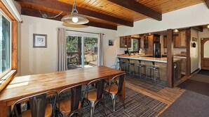 Une cuisine spacieuse avec des poutres en bois, un grand îlot central doté de tabourets de bar et une porte-fenêtre coulissante donnant sur une terrasse.