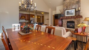 A spacious dining area with a wooden table and chairs, a chandelier, and a stone fireplace. - Ski-In/Ski-Out Penthouse Condo w/ Large Balcony for Gorgeous Slope Views! (Keystone)