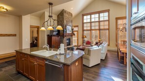 A spacious kitchen with a large island, wooden cabinets, and a stone fireplace. - Ski-In/Ski-Out Penthouse Condo w/ Large Balcony for Gorgeous Slope Views! (Keystone)