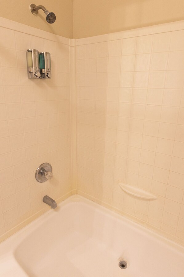 A bathroom with a bathtub, a showerhead, and a soap dispenser.