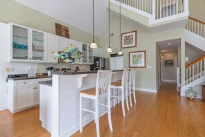 A kitchen with white cabinetry, a central island with bar stools, pendant lighting, and artwork on the walls.