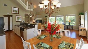 A spacious kitchen with a central island, a dining area with a wooden table and white chairs, and a staircase leading to an upper level.