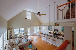 A spacious living area with a high ceiling, a dining table, and a kitchen with white cabinetry.