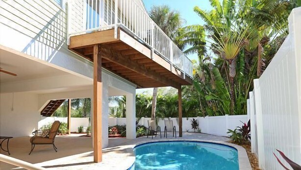 A swimming pool with a wooden deck, a covered seating area, and a view of a house with a balcony.