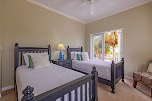 A bedroom with two beds, a nightstand with a lamp, a window with blinds, and a ceiling fan.