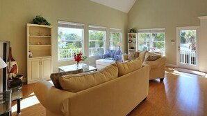 A spacious living room with a high ceiling, large windows, and a balcony.