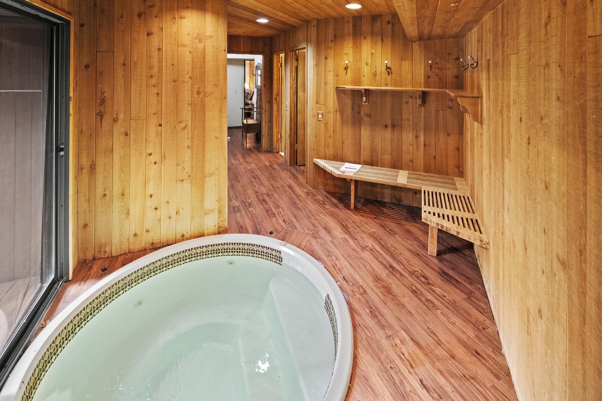 Un espacio tipo spa de madera con un jacuzzi, bancos de madera y un banco con una toalla.