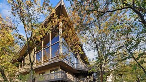 A large, multi-story house with a prominent balcony, surrounded by trees.