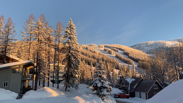 A snow-covered landscape with a cabin, a red truck, and a mountain in the background. - 2 story 3 bedroom Ski condo on Hailey’s run at Whitefish Mountain Resort.  (Whitefish)