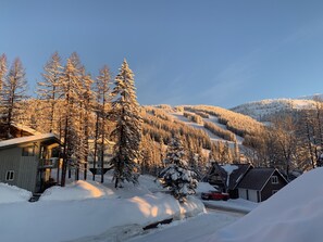 A snow-covered landscape with a cabin, a red truck, and a mountain in the background.