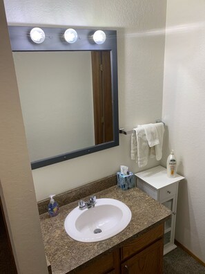 A bathroom with a white sink, a mirror with lights, a towel rack, and a bottle of Jergens Ultra Healing shampoo.