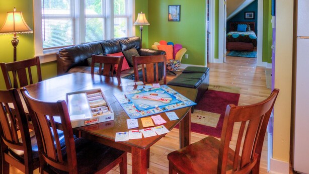 A dining area with a wooden table, chairs, and a board game. There is a leather couch and a small rug in the background.