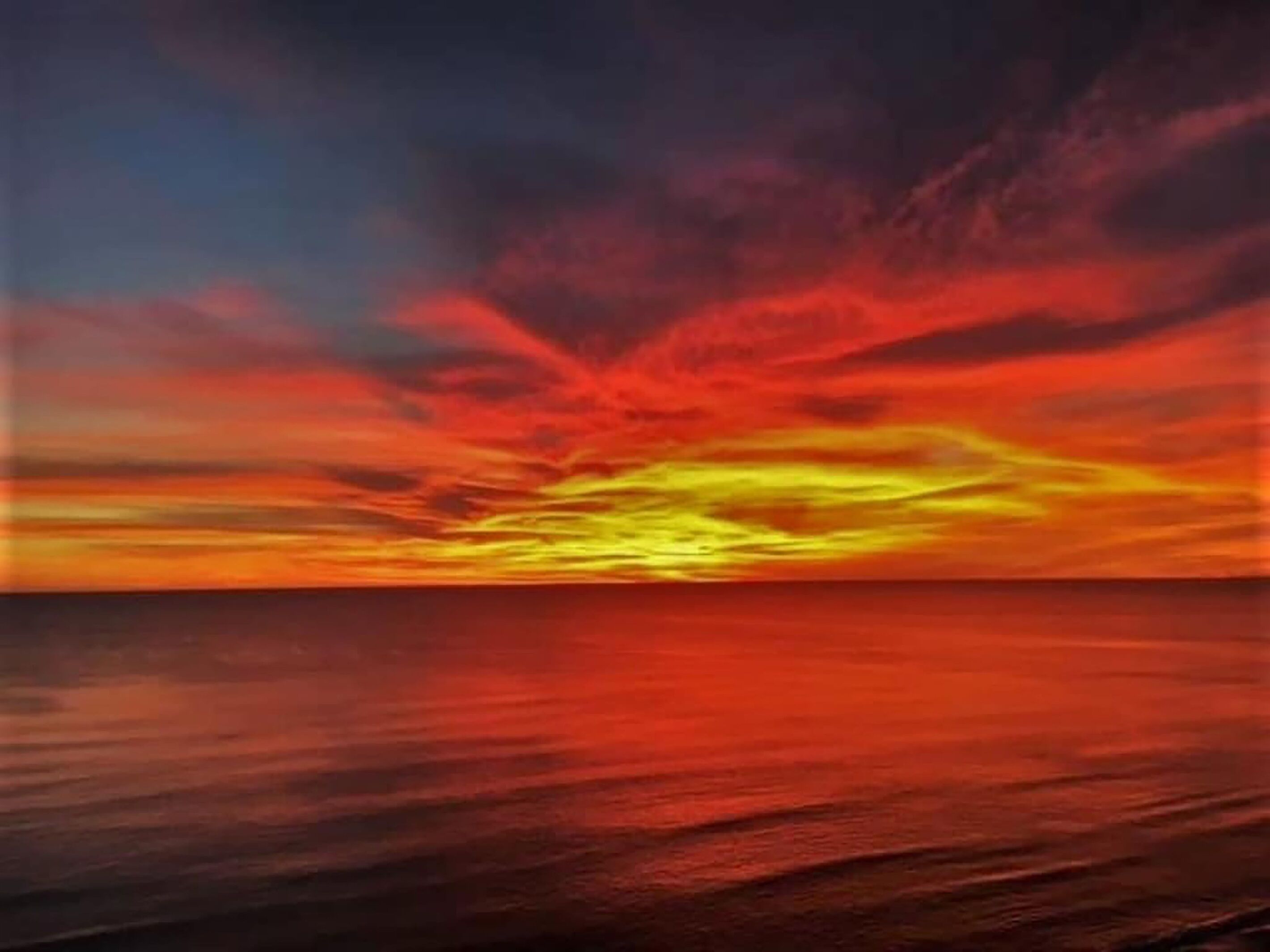 Um pôr do sol sobre um mar calmo, com horizonte nítido.