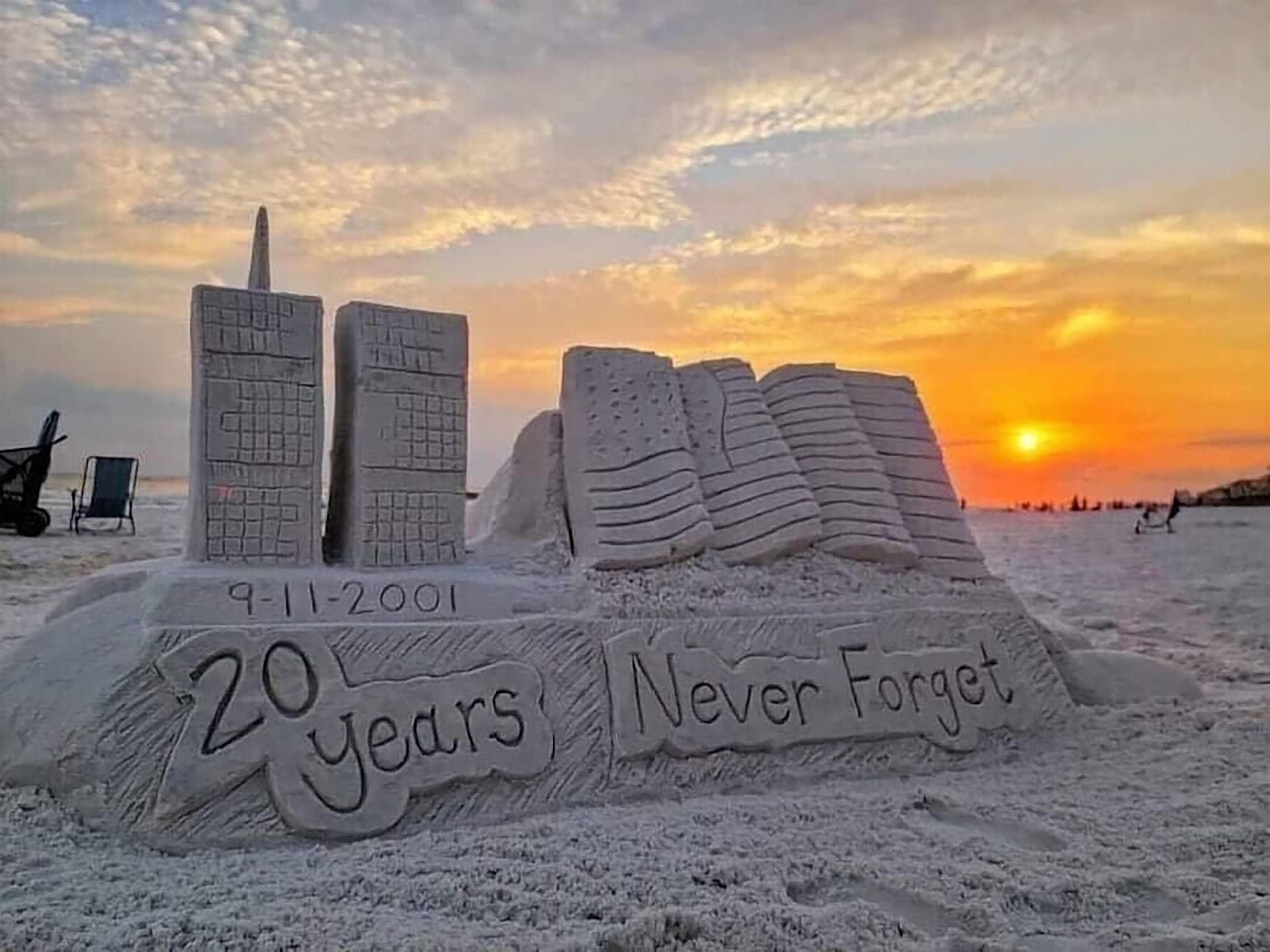 A sand sculpture of buildings and text on a beach at sunset.