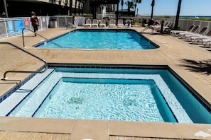 Una piscina rectangular con dos áreas diferenciadas, rodeada de sillones blancos y una terraza con baldosas.