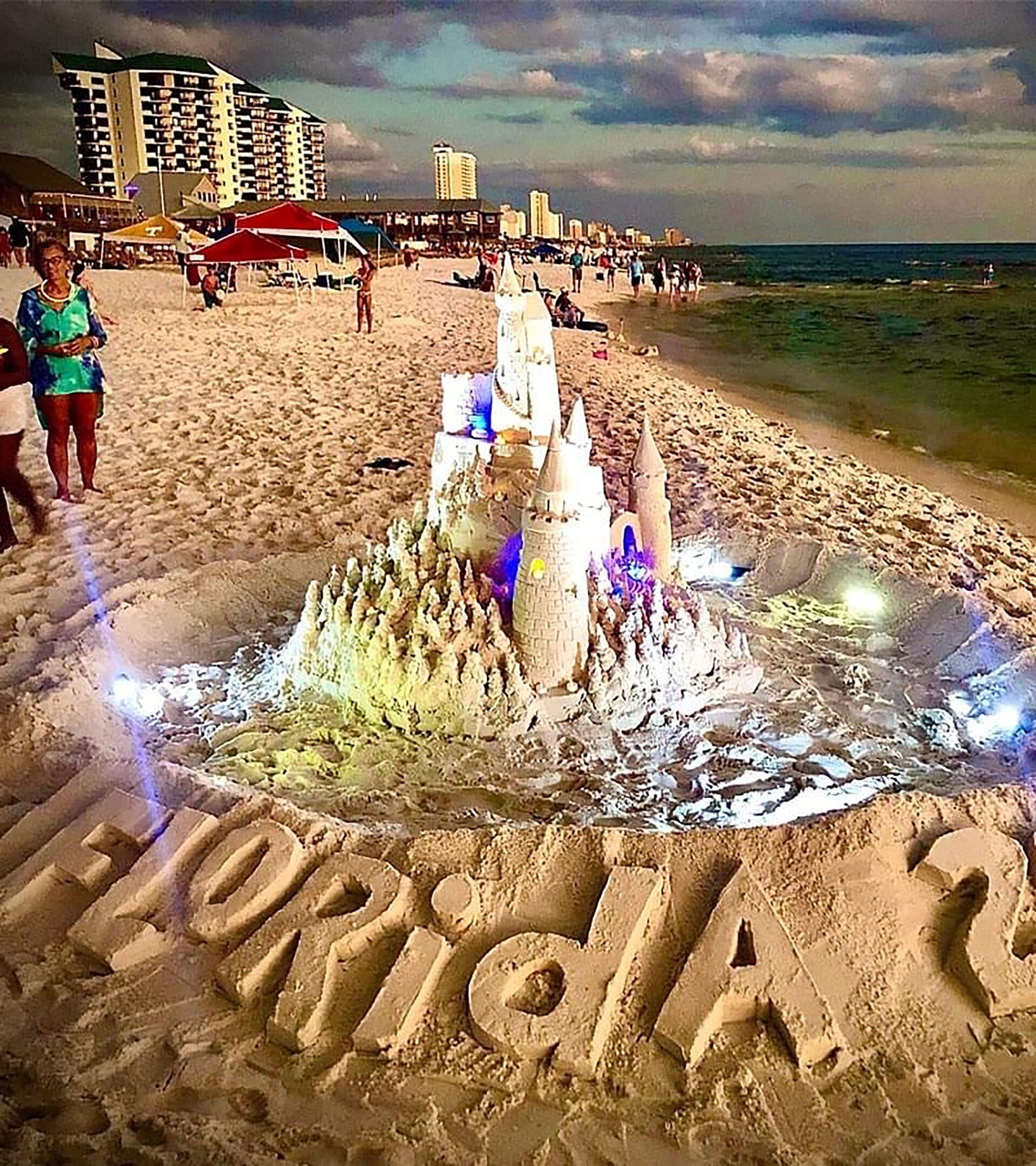 Ein großes Sandkastenschloss am Strand, das Wort "Florida" im Sand geschrieben.