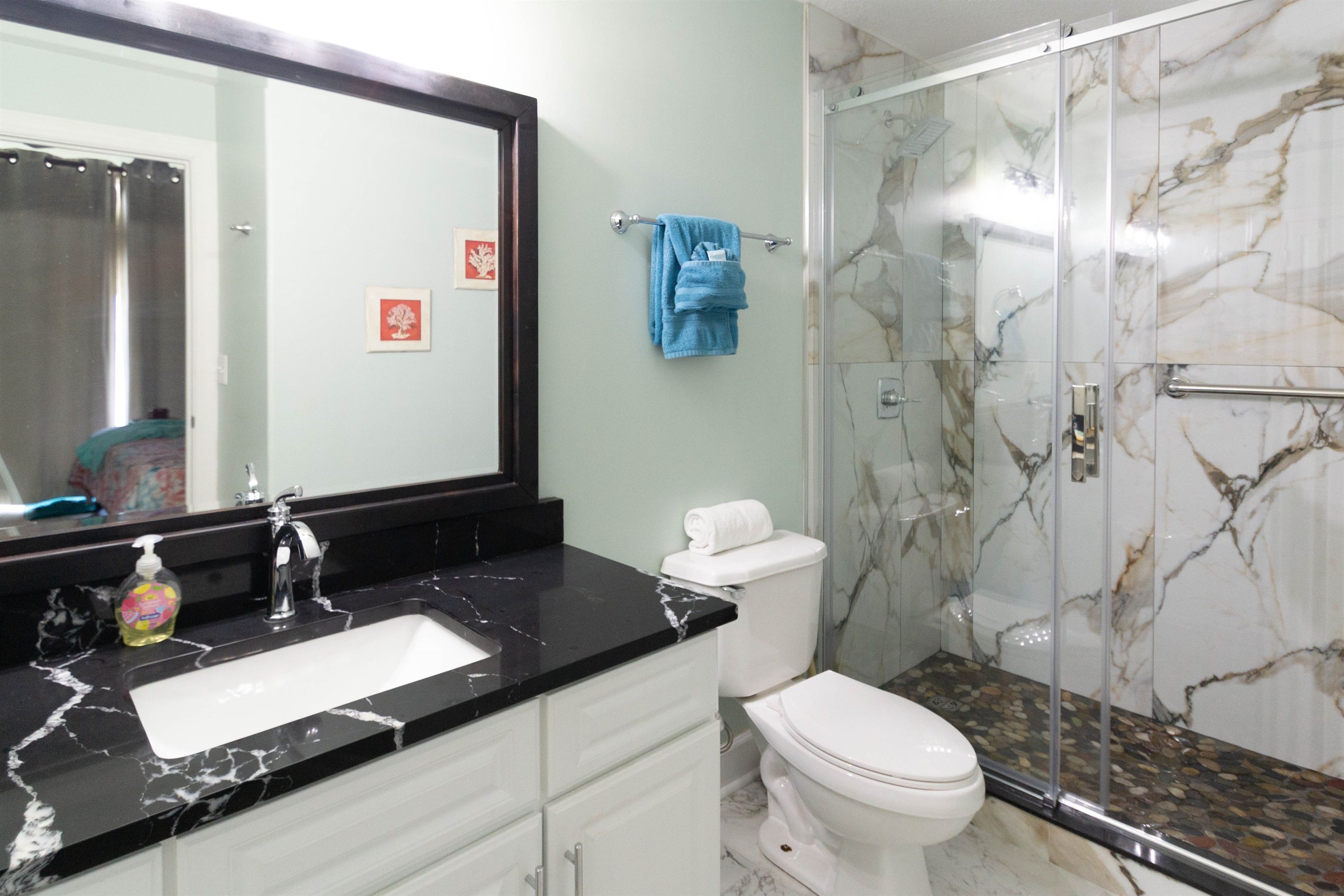 Un baño con lavamanos de mármol negro, inodoro blanco y cabina de ducha de vidrio.