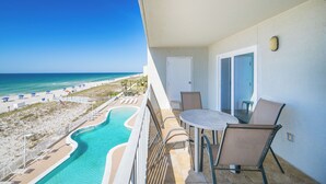 A balcony with a view of a beach and pool, a table with chairs, and a door.