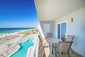 A balcony with a view of a beach and pool, a table with chairs, and a door.