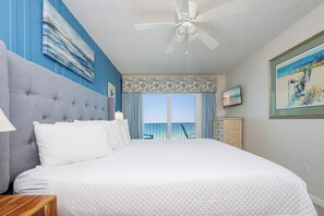 Quarto com cama grande, ventilador de teto, vista para o oceano e varanda.