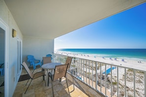 A balcony with a view of the beach, chairs, and a table.