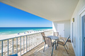 A balcony with a view of the beach, a table, and chairs.