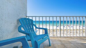 A balcony with a view of a beach, a white textured wall, and a blue plastic chair.