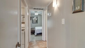 A narrow hallway with a ceiling fan, a bed in the background, and a laundry area to the left. - This is the perfect cozy island bungalow for a weekend of fishing or just hangin (Port Aransas)